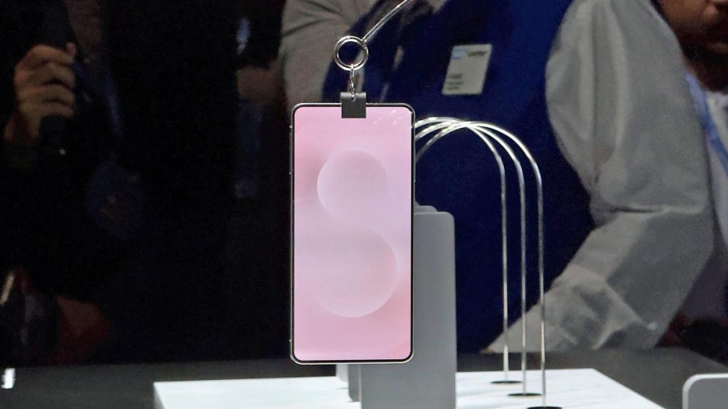 A phone with a pink screen background hangs from a clip on a display floor.