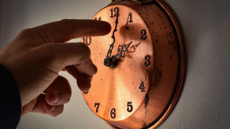 Hand adjusts the time on copper wall clock